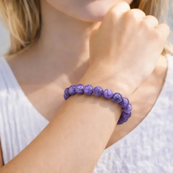 Bracelet en Charoïte naturelle porté au poignet, perles violettes aux volutes nacrées et reflets chatoyants, montage artisanal de luxe.