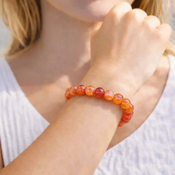 Bracelet en Agate Feu naturelle porté au poignet, perles aux reflets incandescents marron, orange et rouge avec éclats irisés, montage artisanal.