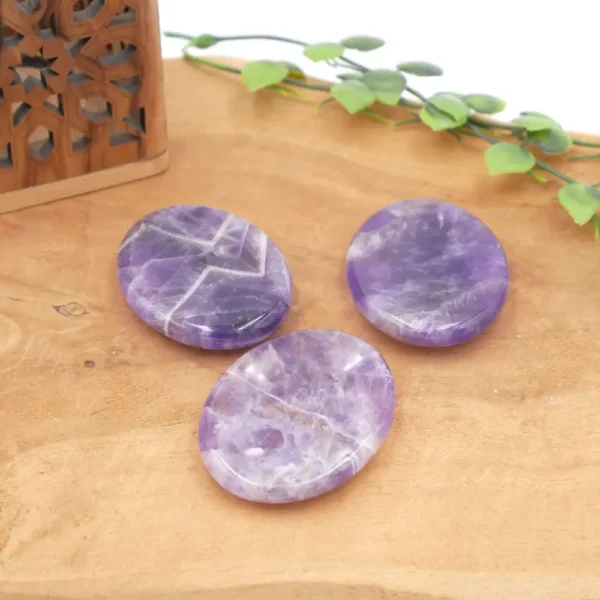 Trois galets plats en améthyste violette avec des veines de quartz blanc, posés sur un support en bois naturel.